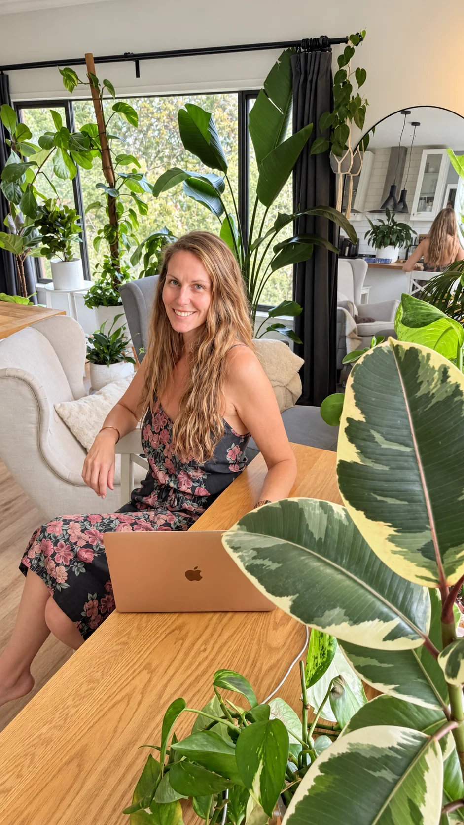 Shelley, the maker of Liana, smiling at her dining table with her laptop, surrounded by her indoor plants